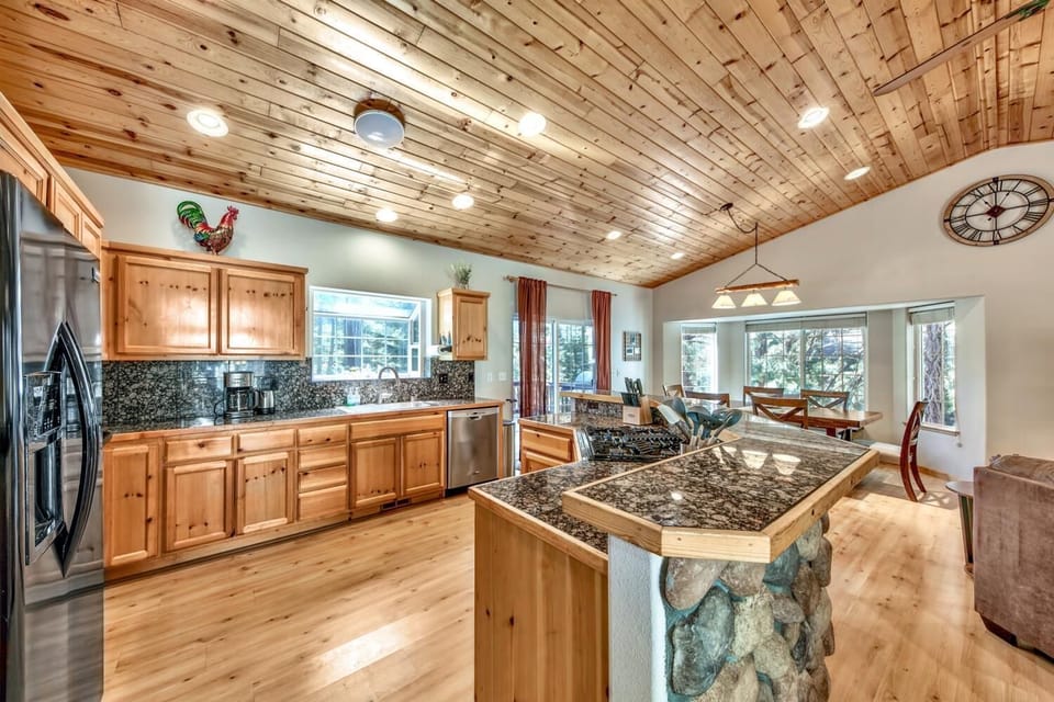 Cook memorable meals in your spacious kitchen featuring rustic wood cabinets, granite countertops, and modern appliances beneath warm knotty pine ceilings.