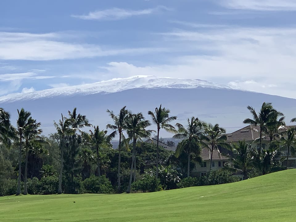 Snowy mountain top view of Mauna Kea while it's 80 degrees at the beach.