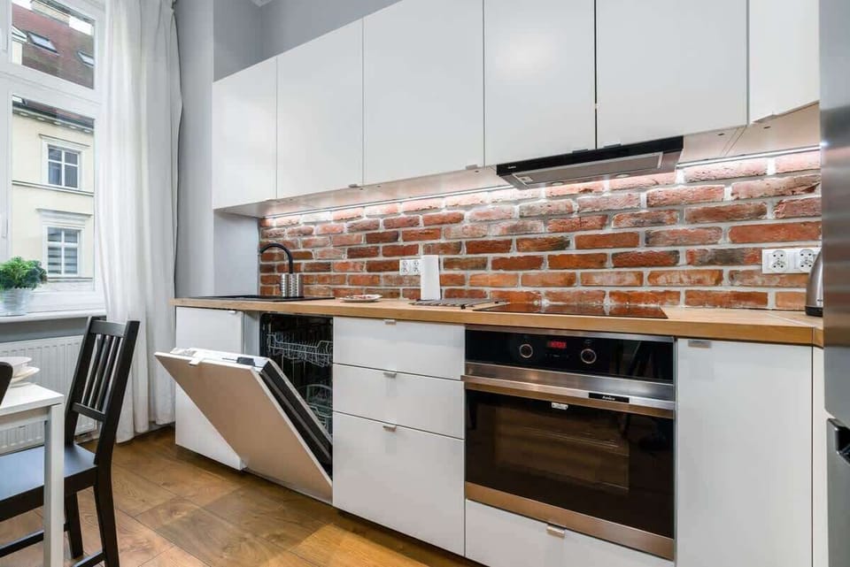Close-up of a modern kitchen with exposed brick backsplash, stove, and cabinets.