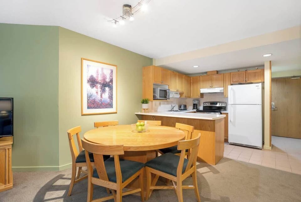 - Bright dining area with wooden furniture and warm mountain charm  
- Open-plan layout ideal for family meals and cozy gatherings  
- Whistler condo living with comfort near trails and ski lifts  