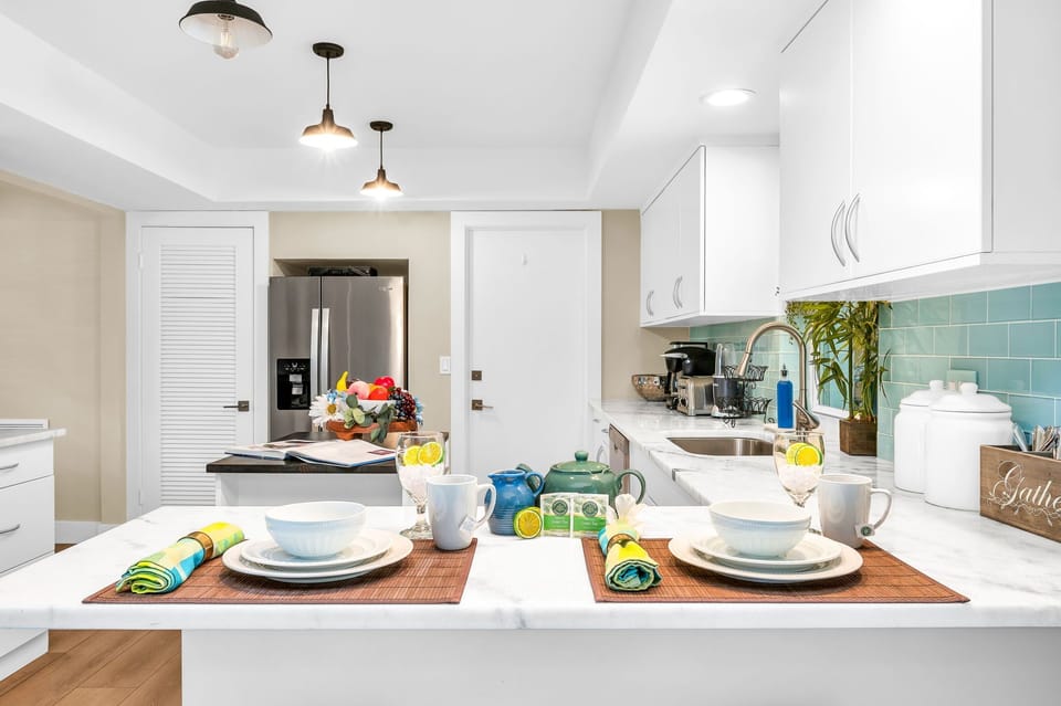 The impressive kitchen is complete with stainless steel appliances and double stainless fridge, a gorgeous aqua tile backsplash, white elegant cabinets, and an island for additonal cooking preparation.