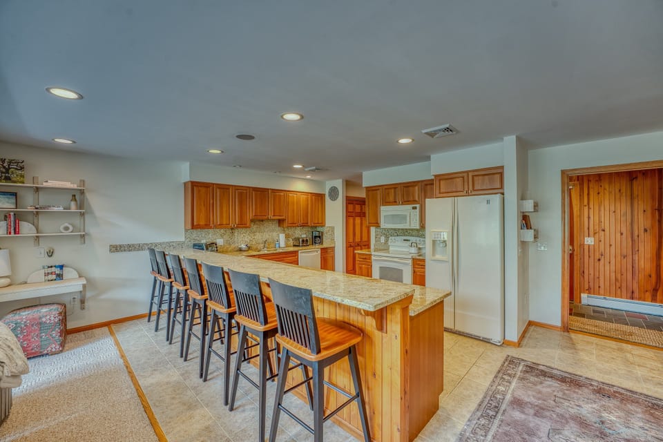 The fully stocked kitchen features warm wood cabinetry, modern appliances, and a large breakfast bar with seating for six