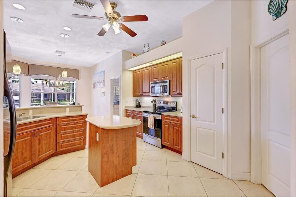 The open plan Kitchen with wooden cabinetry, central island, stainless steel appliances, and large window overlooking the Pool Deck
