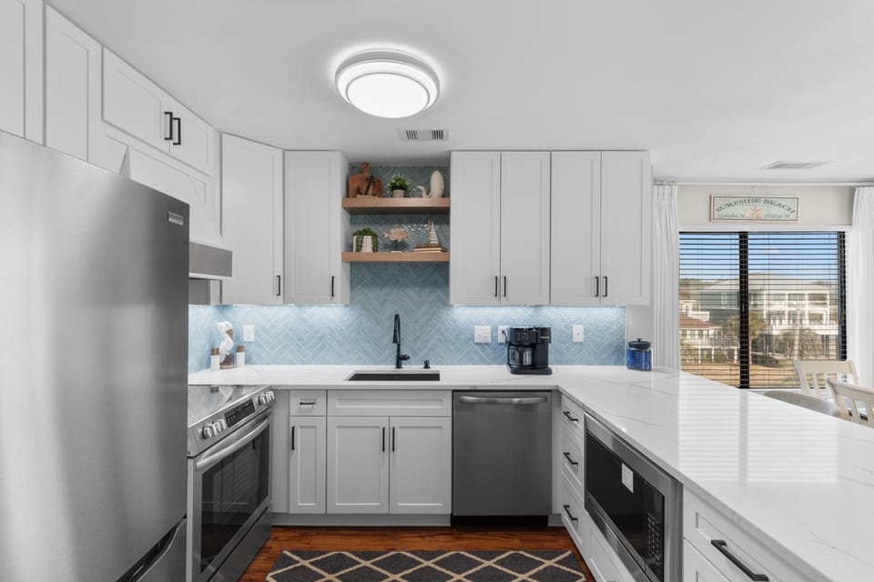 Your fully-equipped kitchen features sleek white cabinets, stainless steel appliances, and a stunning blue herringbone backsplash for memorable coastal cooking.
