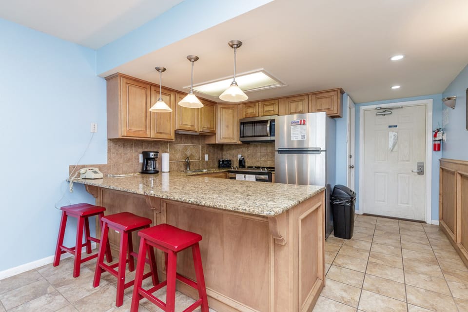 Your fully-equipped kitchen awaits with granite countertops, stainless steel appliances, and cheerful red stools for casual dining.