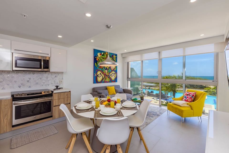 Enjoy meals with sea and pool views from your bright open-plan living space. The modern kitchen, colorful decor, and sunlit dining area create a welcoming coastal retreat.