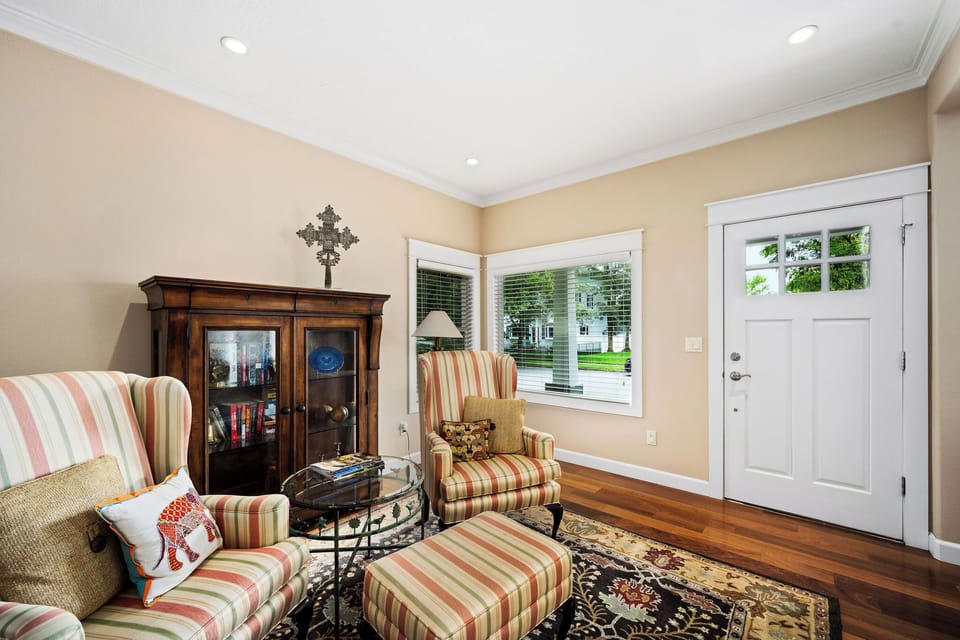 Sink into comfortable striped armchairs by the sunny window, where warm hardwood floors and cozy furnishings create your perfect reading retreat.