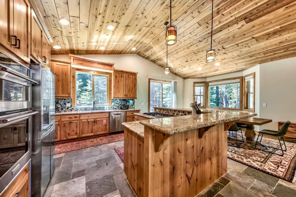Your rustic-modern kitchen awaits with gleaming granite counters, warm wood cabinets, and forest views through every window.