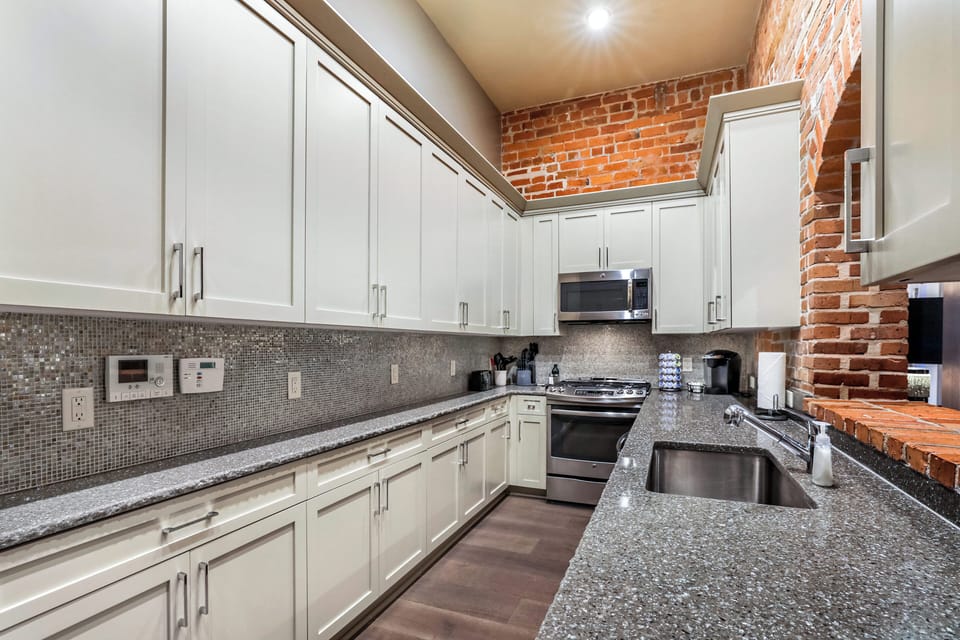 Galley-style, fully equipped kitchen with open flow to living/dining area. Fully stocked with essentials, from mixing bowls to wine glasses. Features stainless steel appliances, gas range, stone countertops, tile backsplash for a luxurious feel!