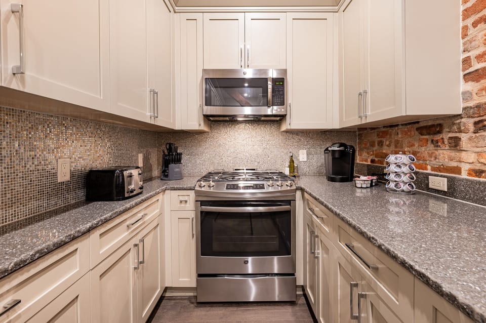 Side 2: Galley-style, fully equipped kitchen with open flow to the living/dining area. Stocked with essentials from mixing bowls to wine glasses, featuring stainless steel appliances, stone countertops, and a tile backsplash for a luxurious touch!