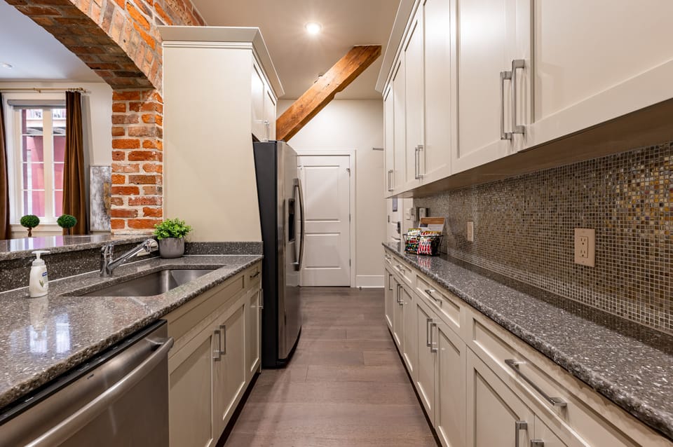 Side 2: Galley-style, fully equipped kitchen with open flow to the living/dining area. Stocked with essentials from mixing bowls to wine glasses, featuring stainless steel appliances, stone countertops, and a tile backsplash for a luxurious touch!