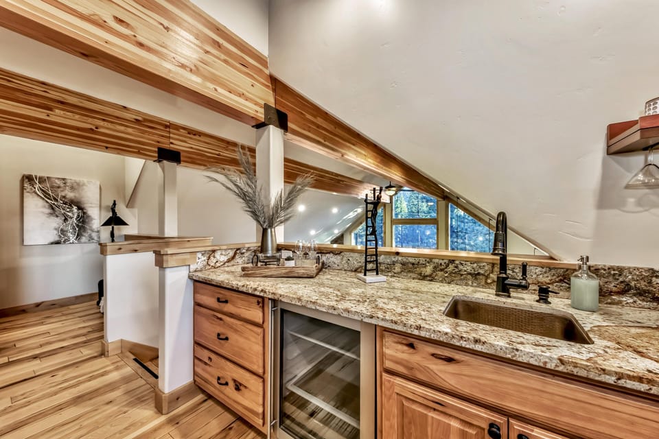 Granite countertop with undermount sink and black faucet sits beneath sloped ceiling and wood beams.