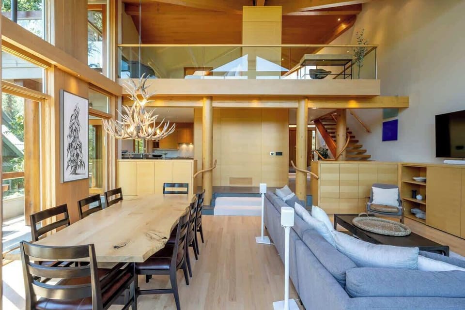 - Open-concept design with warm wood accents and high ceilings  
- Elegant dining area beside cozy lounge and stone fireplace  
- Ideal for family gatherings in a bright alpine retreat  