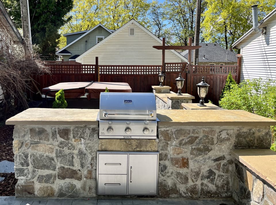Fully fenced backyard has built in grill with stonework, lighting, and hot tub