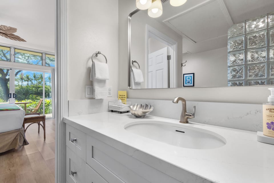 Refresh in your bright, spa-like bathroom with elegant counters, soft lighting, and a glimpse of tropical greenery just outside your window.