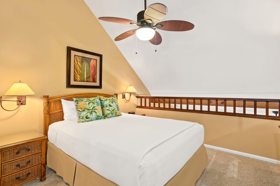 Your tropical-inspired retreat features a plush bed beneath soaring ceilings and a charming ceiling fan. Warm tones and wicker furniture invite you to unwind in island-style comfort.