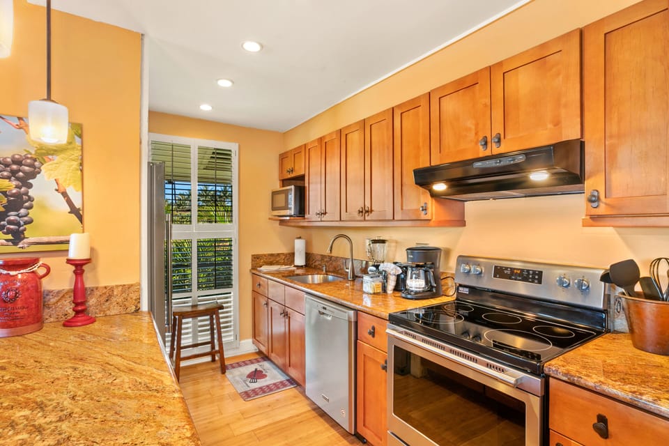 Prepare your favorite meals in this fully-equipped kitchen featuring warm wood cabinetry, granite countertops, and stainless steel appliances—all bathed in natural light from sunny windows.