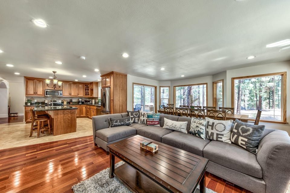 Open-plan living area features a gray sectional with decorative pillows and a dark wood coffee table on hardwood floors.