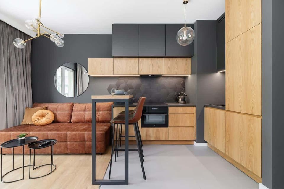 A modern open-plan living room featuring a comfortable sofa, dining table, and integrated kitchen with wooden and black cabinetry.