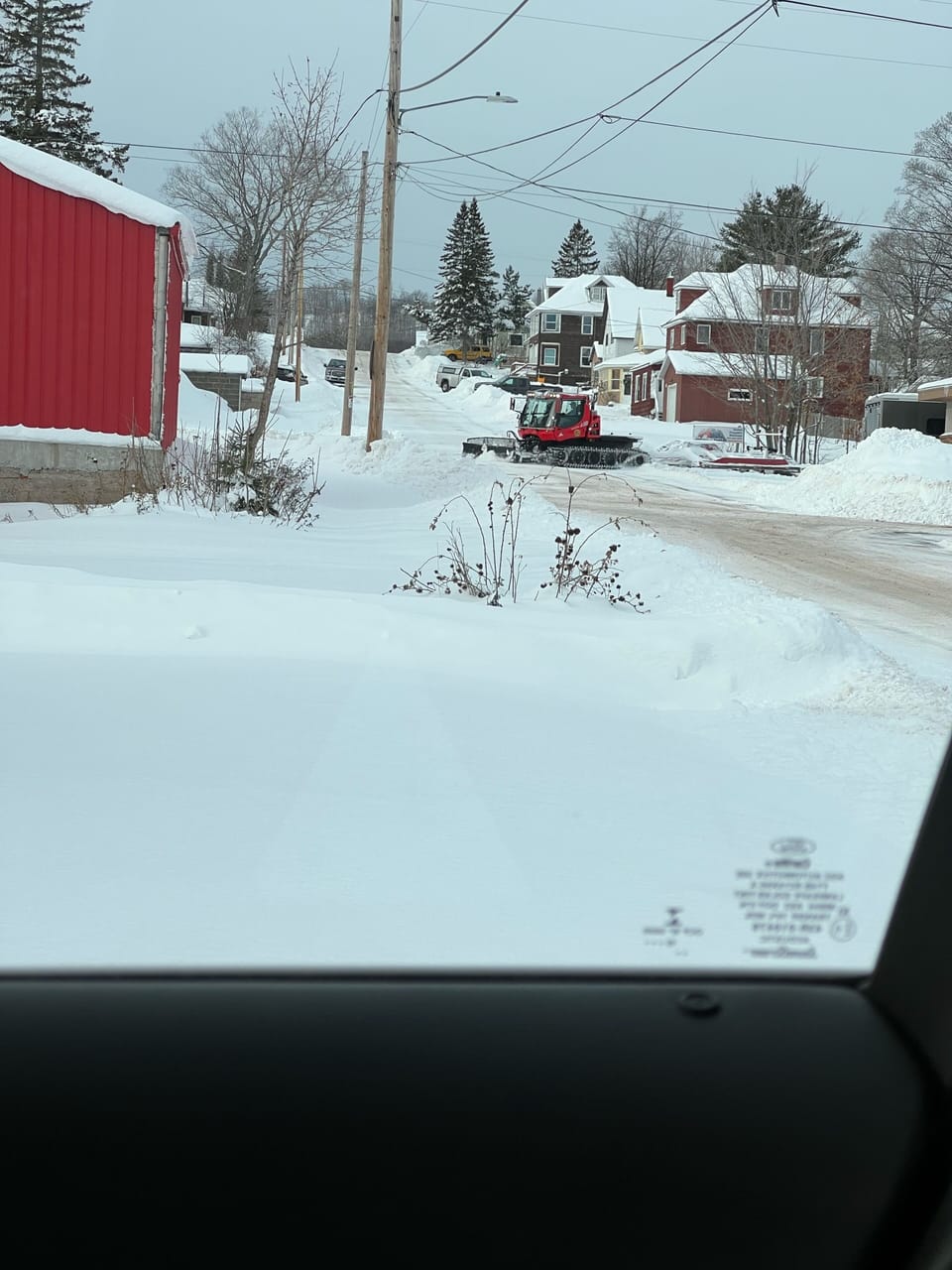 A view from the front yard of snowmobile trail groomer  grooming the trail.  