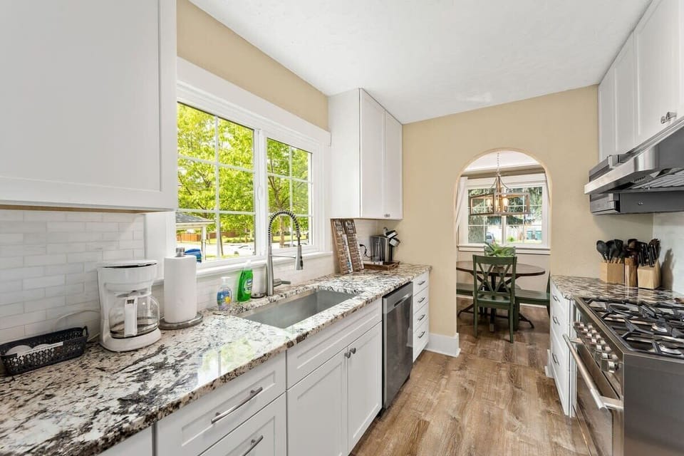 Your fully equipped kitchen awaits with granite counters, modern appliances, and sunny windows overlooking leafy trees for inspired home cooking.