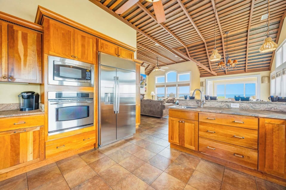 Warm wood cabinetry and modern stainless appliances set the stage for your culinary adventures, all under a stunning barrel-vault ceiling with breathtaking ocean views beyond.