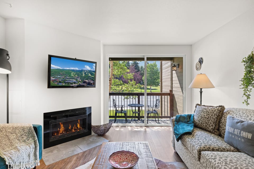 The living room offers a gas burning fireplace, flatscreen TV, and two colorful couches.
