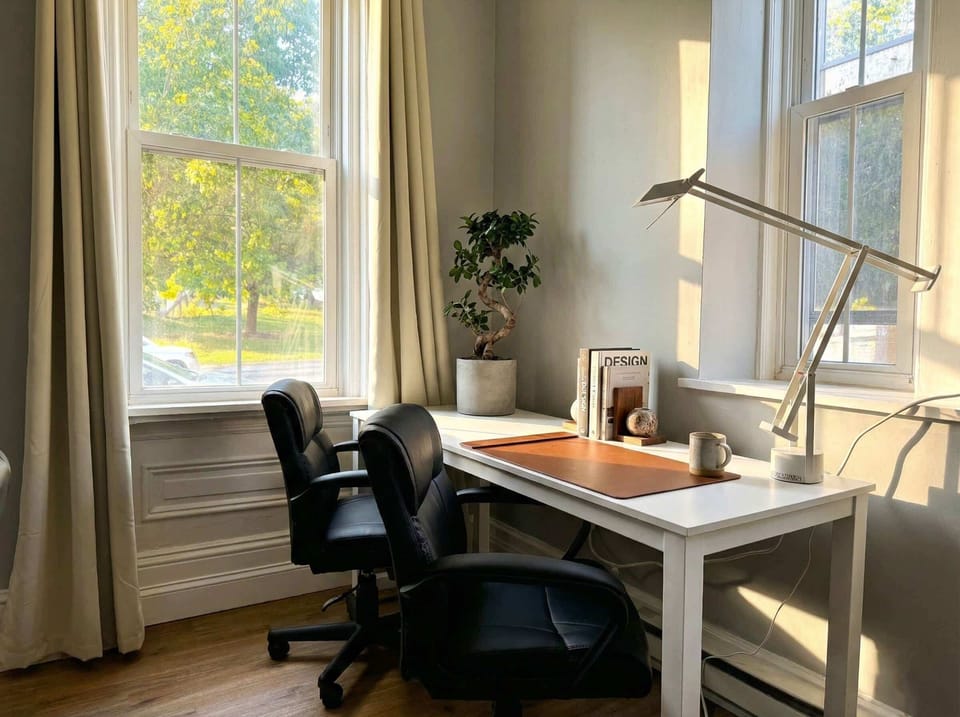 Dedicated workspace with desk, office chair, task lamp, and natural light from large windows.
