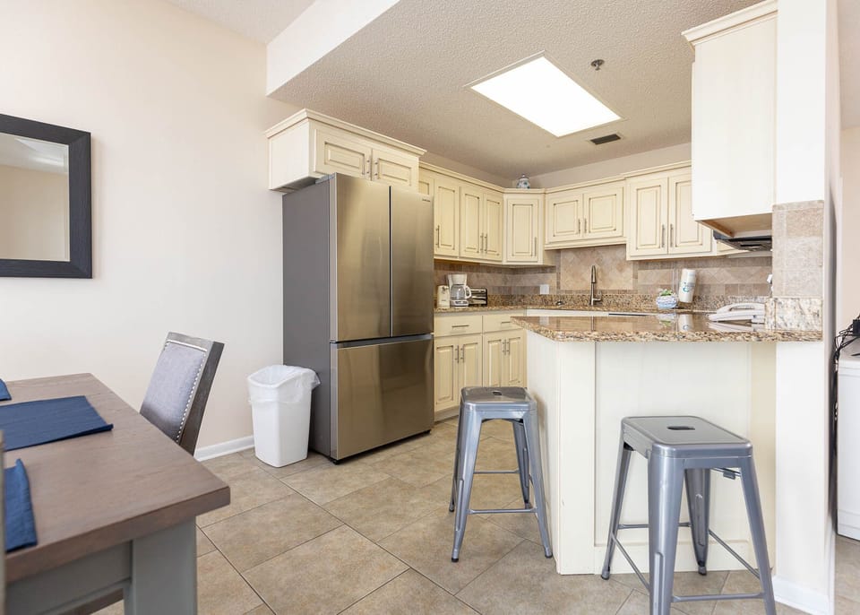 Modern kitchen features light cabinetry, granite countertops, and a breakfast bar with stools for casual dining