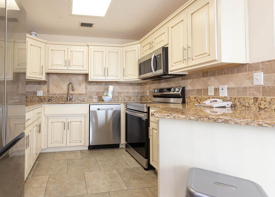 Bright kitchen features cream-colored cabinetry, granite countertops, and stainless appliances, perfect for preparing meals