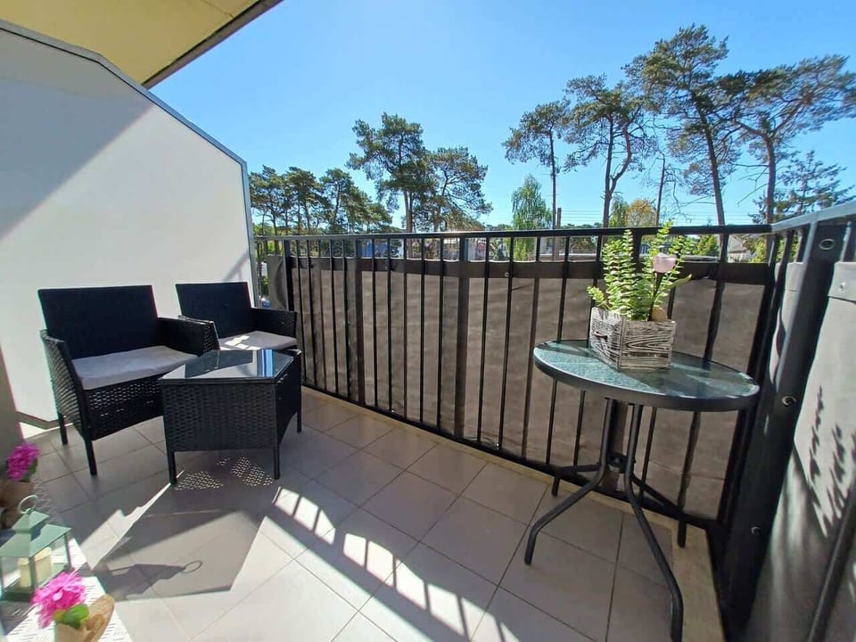 A stylish balcony with a metal table and chairs, overlooking trees, combines simplicity with nature.
