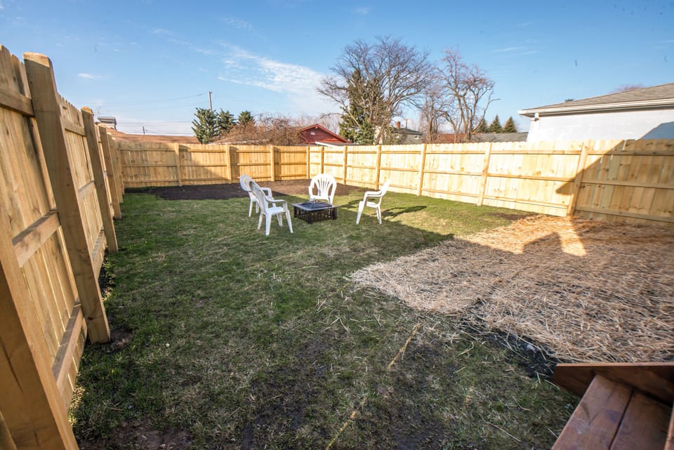 Fully fenced yard with fire pit and chairs.