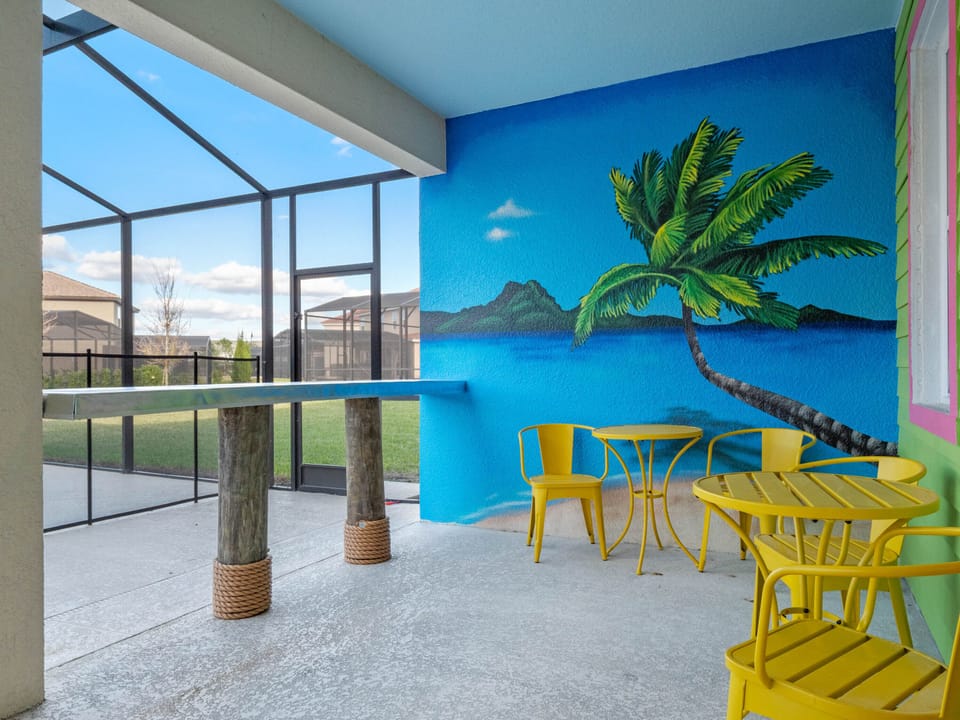 - Covered outdoor seating with tropical mural backdrop  
- Bright yellow chairs and palm tree artwork design  
- Relax by the poolside in this Orlando rental home