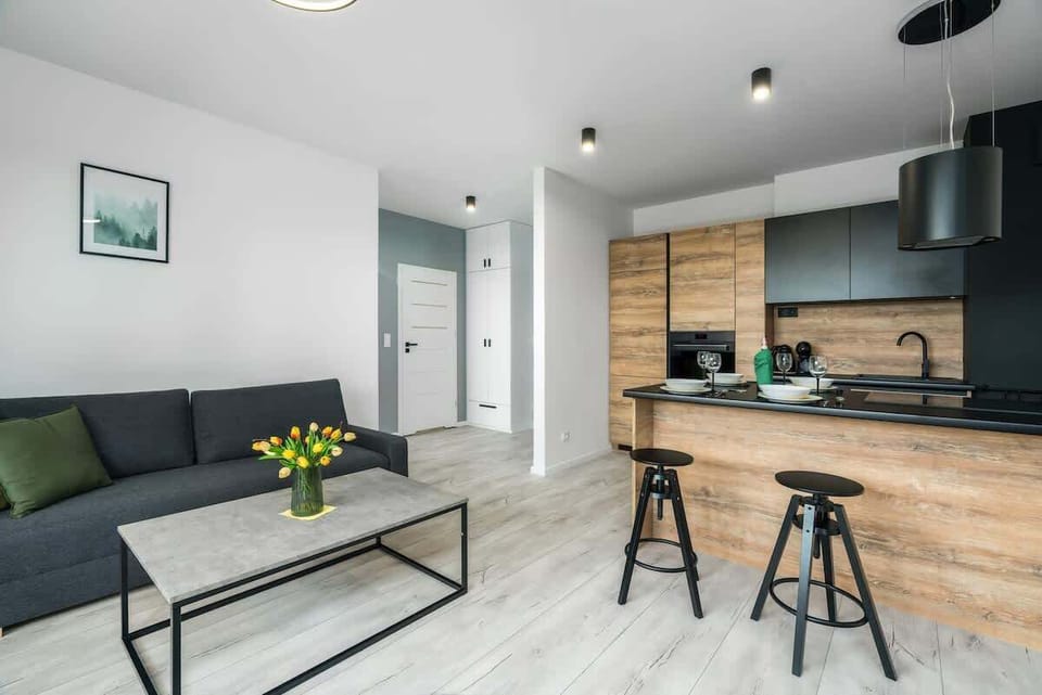 An open-concept area combining the living room and kitchen, featuring a minimalist design with natural wood tones, a grey sofa, and a bright atmosphere.