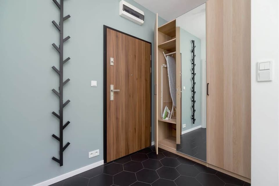 The apartment’s entryway with a wooden wardrobe, a sleek black coat hanger, and geometric floor tiles.