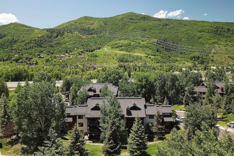 Aerial view of mountain valley property nestled among lush green hills and ski slopes, surrounded by natural forest landscape.