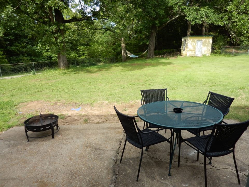 Fenced-in backyard, patio set, firepit, hammock, forest setting
