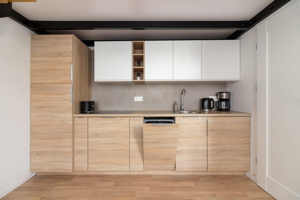 A compact kitchenette with modern wooden cabinets, white countertops, and essential appliances.