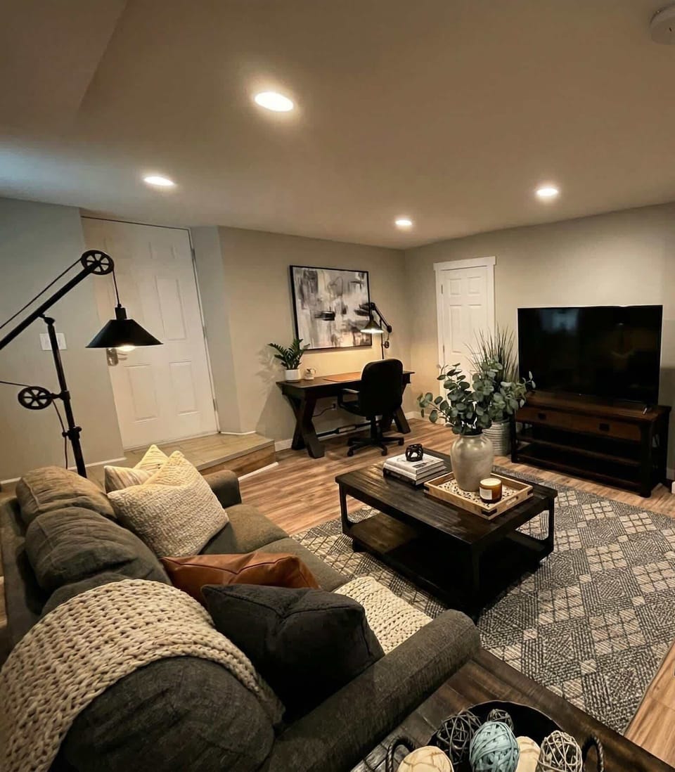 Living room with sofa seating, coffee table, TV, desk, and plants.