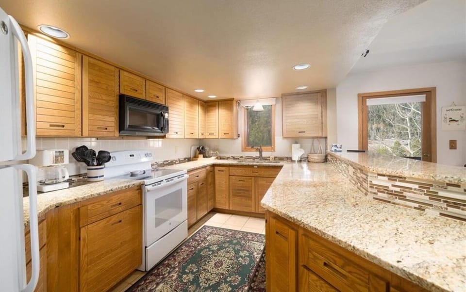 A kitchen with wooden cabinets, white appliances, and a granite countertop. A patterned rug is on the floor, and a window and a wooden door are on the far wall.
