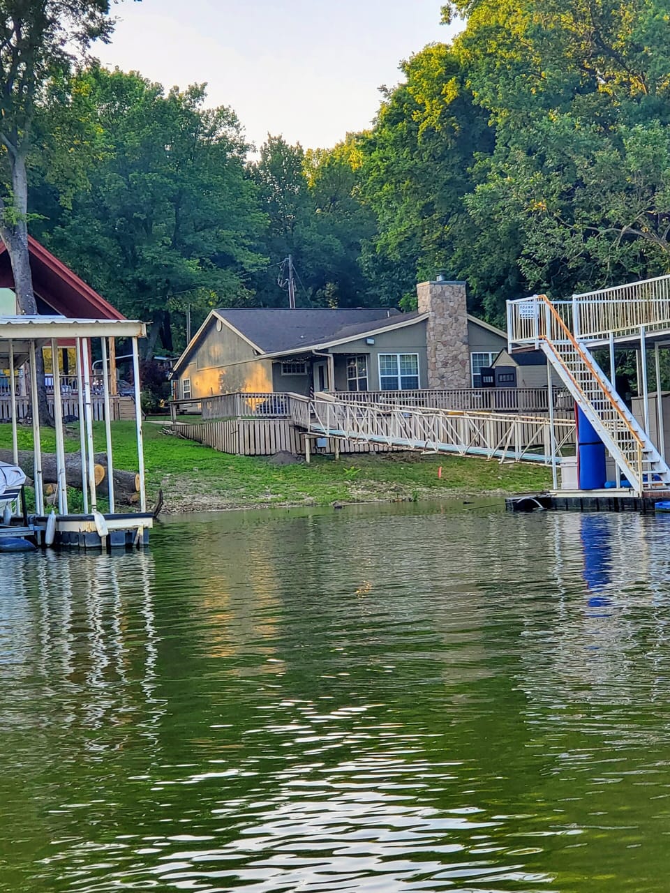 Photo of house, walkway, and dock from lake. Stairs going up to veranda.
