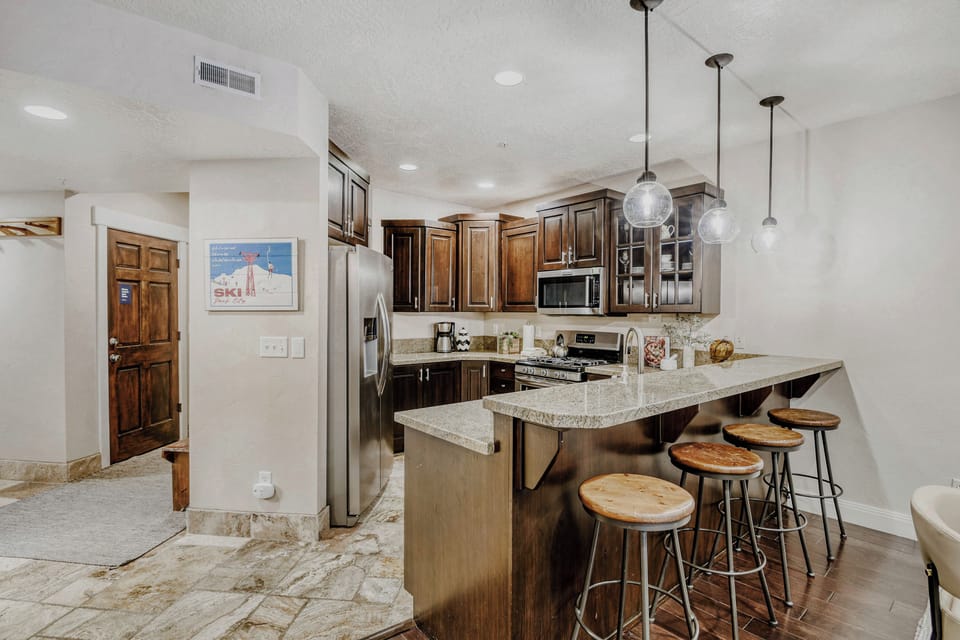 Your fully equipped kitchen features rich wood cabinetry, granite countertops, stainless steel appliances, and a breakfast bar with seating—perfect for preparing meals and gathering with friends.