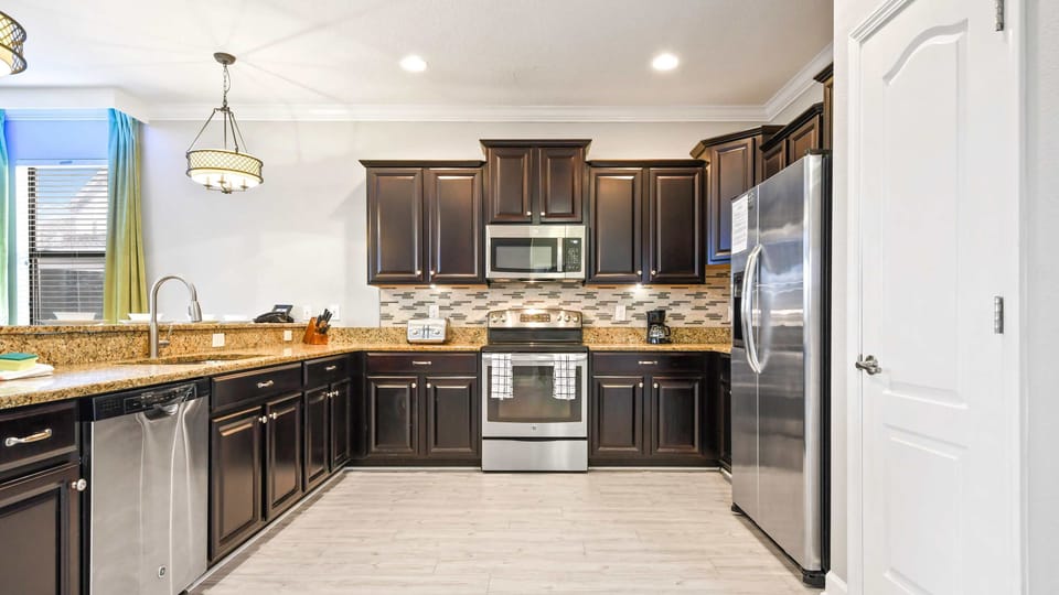 Sleek kitchen with dark wood cabinets, stainless steel appliances, granite countertops, and modern lighting.