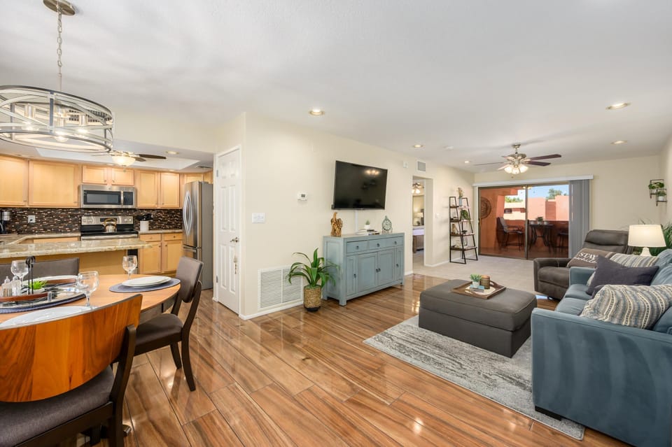 Open living and dining area with polished wood floors, blue sofa, gray ottoman, and sliding glass door to balcony.