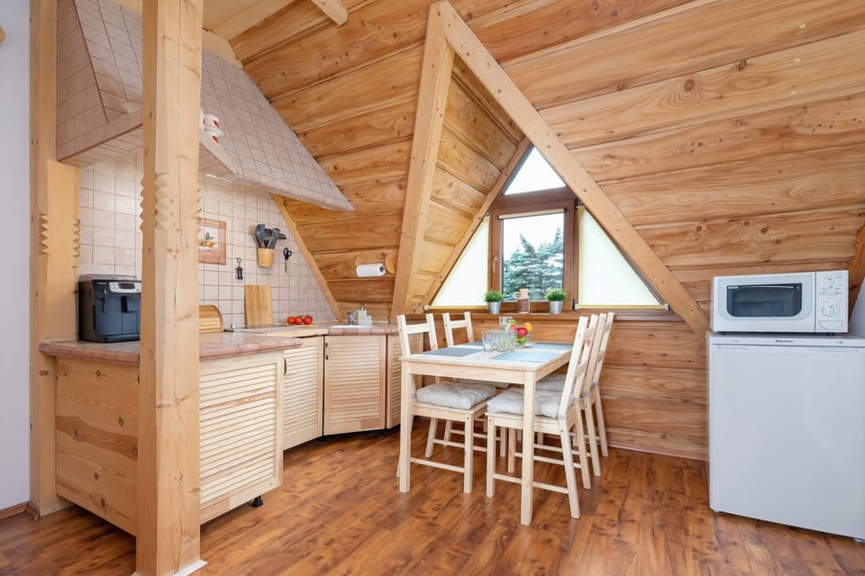 A compact kitchen and dining nook made entirely of light wood, with a rustic dining table and chairs under the sloped ceiling.