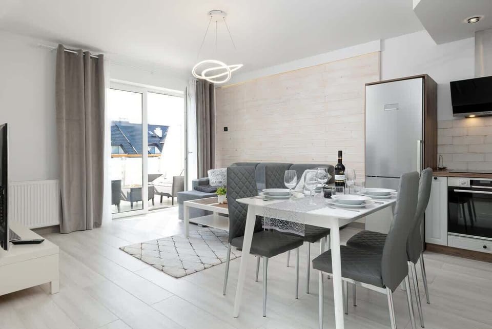 A wide view of the open-plan living area, featuring a dining table set for four and a TV unit for entertainment.