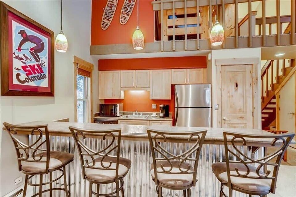 Fully-stocked kitchen with four bar stools and stairs to the second floor