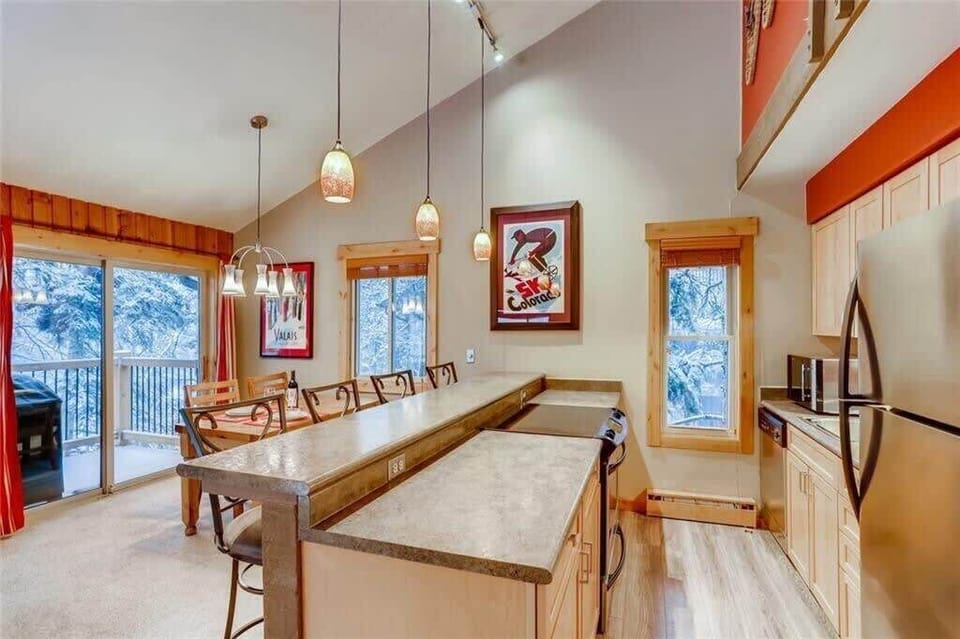 View of the fully-stocked kitchen with four bar stools, dining area, and outdoor deck