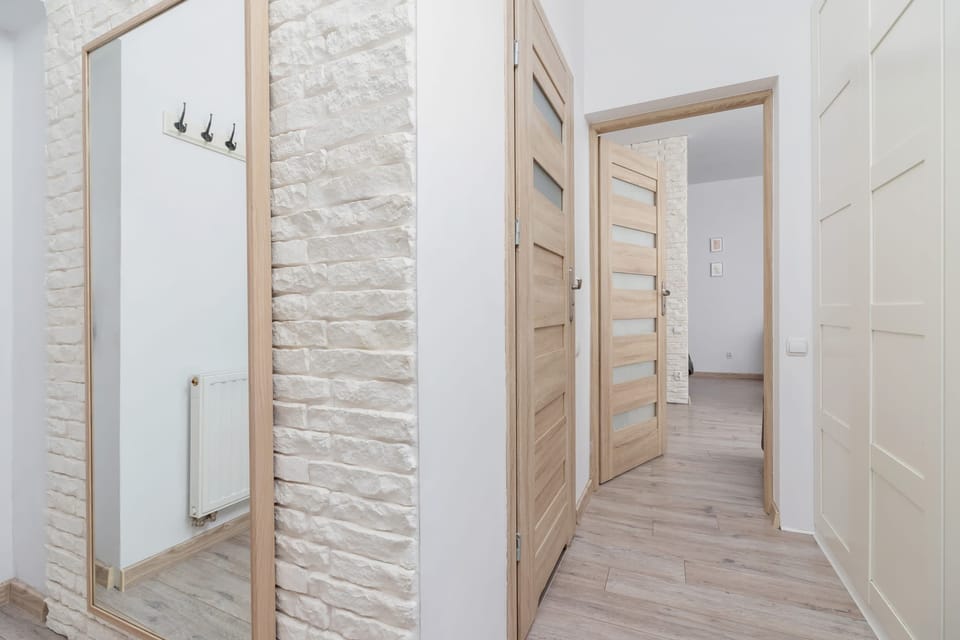 A corridor with a tall mirror on the wall and light wood flooring.