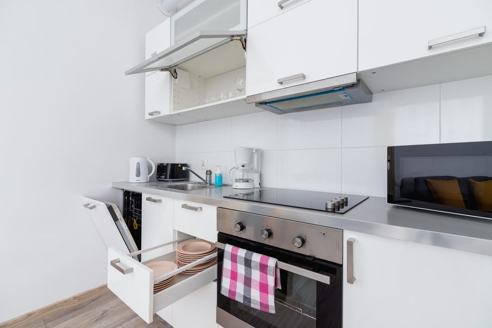 A compact kitchen with modern appliances, white cabinetry, and a black countertop.